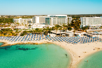 Ayia Napa, Cyprus - 15th april, 2023: aerial fly over Luxury hotel buildings with pools by beach with island greenery panorama.White sand most famous in Cyprus - Nissi beach