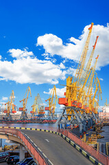 Naklejka premium A row of large yellow industrial cranes at a seaport dock with water in the foreground and city buildings in the background. Odessa, Ukraine.