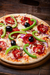 Pizza with chorizo ​​sausage, mozzarella cheese, green pepper and black olives. Rustic wooden background. Soft focus.	