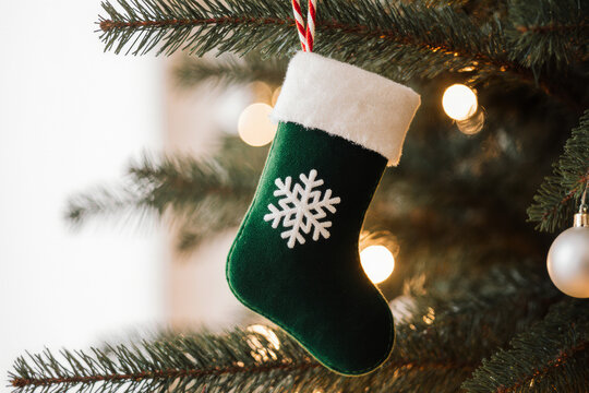 Festive green Christmas stocking with snowflake ornament hanging on a decorated evergreen tree with blurred lights