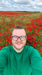 A smiling Caucasian man revels among vivid poppies, evoking Beltane celebrations and hidden tales...