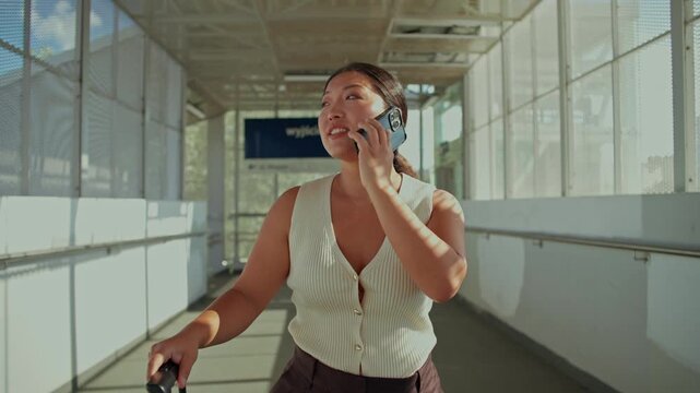 A woman is talking on a mobile phone walking along the passage at the train station.