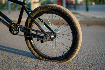 A BMX bicycle rests on a city street with a flat rear tire, highlighting the punctured condition...