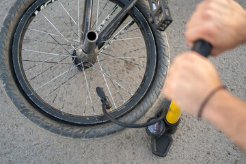 Rider uses a hand pump to inflate the tire of a BMX bicycle on a gravel surface with sunlight...
