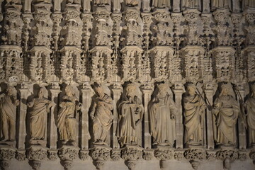 This is a close-up of a stone facade from the Seville Cathedral. The photo shows a row of intricately carved statues of religious figures, set beneath a highly decorated, Gothic-style canopy.