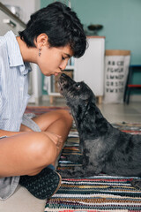 Young girl kissing her adorable black dog at home