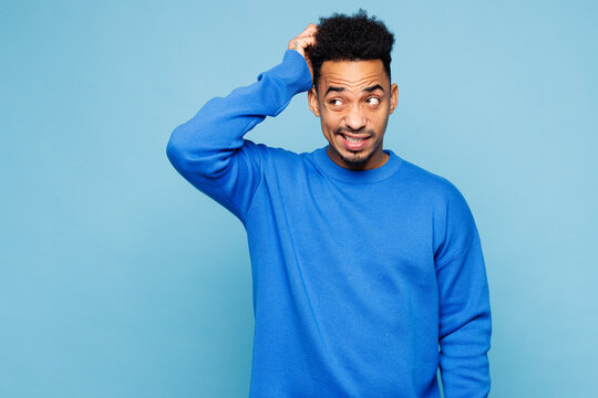 Young sad man of African American ethnicity he wear sweatshirt casual clothes put hand on head scratch temple look aside isolated on plain pastel light blue cyan background studio. Lifestyle concept. - Powered by Adobe