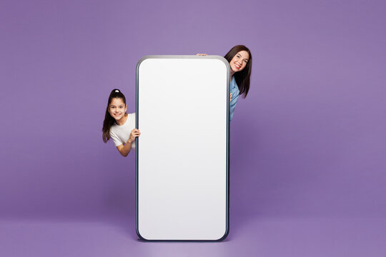 Fototapeta Full body young woman child baby girl 8-9 years old wear blue casual clothes. Mommy little kid behind big huge blank screen mobile cell phone isolated on plain purple background Mother's Day concept.