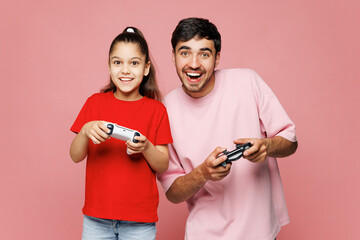 Young happy parent man with child girl wear red casual clothes. Daddy little kid daughter hold play pc game with joystick console isolated on plain pink background. Father's Day Love family concept. © ViDi Studio