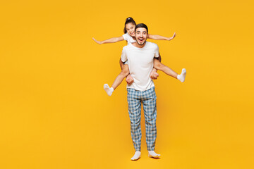 Full body young happy fun parent man with child girl wear blue pyjamas clothes. Daddy little kid giving piggyback ride to joyful isolated on plain yellow background. Father's Day Love family concept.