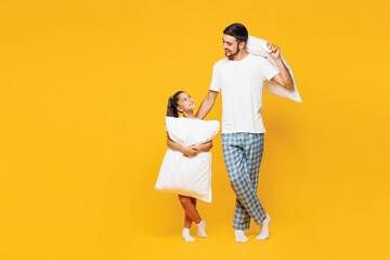 Full body young parent man with child girl wear casual blue pyjamas clothes. Daddy little kid daughter hold pillow going to sleep isolated on plain yellow background. Father's Day Love family concept.