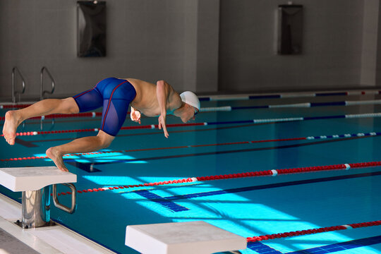 Male swimmer diving into pool in dynamic start motion. Concept of competitive sports, speed, motivation, training, technique, and determination with focused emotion.