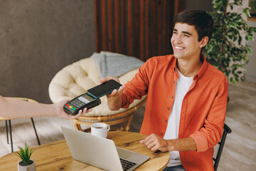 Young man he wears casual clothes hold bank payment terminal process acquire cell phone sit at table in coffee shop cafe relax rest in restaurant in free time indoor Freelance mobile office concept.