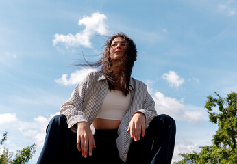 Beautiful young woman sitting on a bench under the blue sky, low angle view