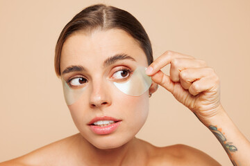 Beautiful half naked topless young woman 20s with nude make up wearing patch under eye isolated on plain beige color wall background studio portrait. Skin care healthcare cosmetic procedures concept.