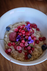 oatmeal porridge with red frozen berries and violet flowers