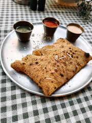 Delicious flatbread served with green sauce, tamarind sauce, and yogurt on a checkered table