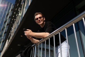 Young man using smartphone on balcony of modern building during sunny day