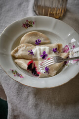 Dumplings with blueberry filling with addition of cream on a white plate, top view. Traditional home dish