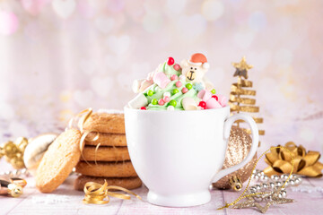 Festive tasty Christmas hot chocolate with green and red colored whipped cream, with marshmallow and sugar holiday decorations on top, on festive holiday decorated  background