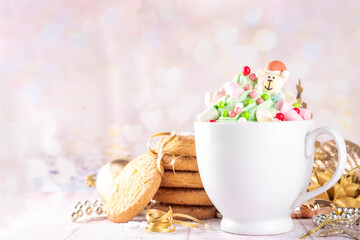 Festive tasty Christmas hot chocolate with green and red colored whipped cream, with marshmallow and sugar holiday decorations on top, on festive holiday decorated  background