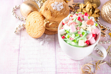 Festive tasty Christmas hot chocolate with green and red colored whipped cream, with marshmallow and sugar holiday decorations on top, on festive holiday decorated  background