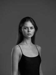 Fototapeta premium Black and white portrait of a serious woman with long hair in a dark top on a plain background