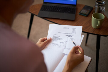 Middle aged Caucasian woman reviewing financial document while sitting at table, holding paper in...