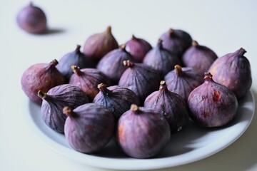 A close-up of a pile of fresh, ripe figs on a clean white plate, representing a natural and wholesome autumn harvest ready to be enjoyed.