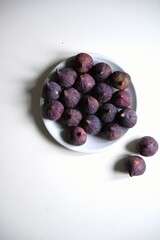 A top-down shot of a pile of fresh, ripe figs on a clean white plate, representing a natural and nutritious snack or a wholesome ingredient for a healthy diet.