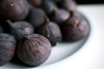  A beautiful close-up of fresh, ripe figs on a clean white plate, with a shallow depth of field to highlight the rich color and texture, perfect for a culinary illustration.