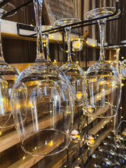 Upside-down wine glasses hang neatly on a rack, illuminated by twinkling decorative lights.