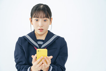 スマホを見て驚くセーラー服を着た女子学生