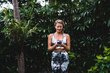 Woman in activewear sitting with smartphone, immersed in digital world amid nature. Concept of...