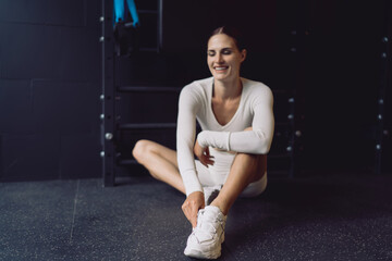 Naklejka premium Cheerful woman smiling after workout, stretching legs and adjusting shoes, capturing joyful balance between discipline and ease in personal fitness practice.