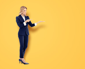Full body image - cute smile businesswoman woman wear black corporate suit, pointing showing giving demonstrating. Business ad concept. Isolate orange yellow background with free text space