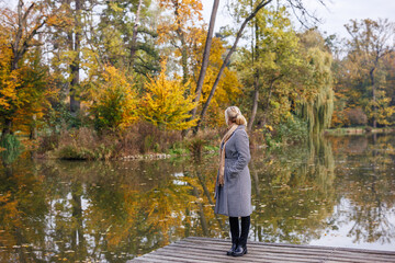 Woman in houndstooth coat standing by lake in autumn park. Fall season fashion lifestyle