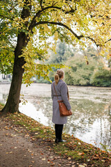 Pensive woman standing in autumn park, expressing melancholy and thoughtful mood