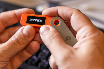 hardware Bitcoin wallet in a hands with message BANNED on screen