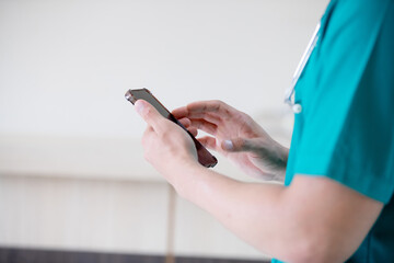 Male doctor wearing lab coat holding cellphone beside windows in hospital