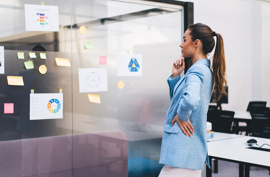 Thoughtful freelancer in blue blazer analyzing colorful sticky notes, demonstrating strategic analysis, prioritization and tech-driven decision-making in creative business context.