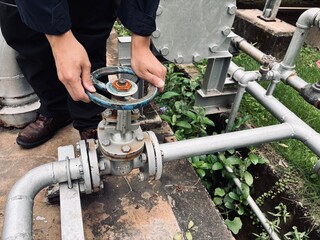 Engineer operating industrial valve on pipeline system in outdoor facility.