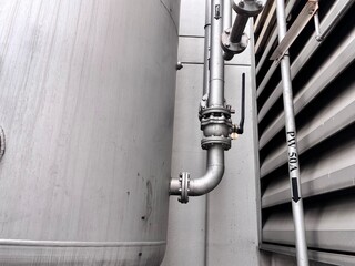 Close-up of industrial piping, valves, and flange connections on the side of a large storage tank...