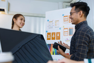 A man and two women are sitting at a table with a white background. The man is drawing on a white board while the women look on. Scene is collaborative and creative
