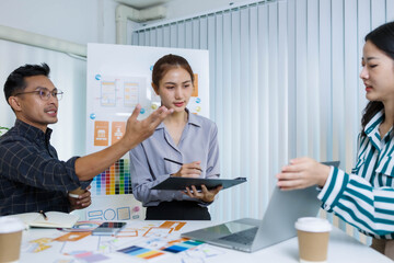 A man and two women are sitting at a table with a white background. The man is drawing on a white board while the women look on. Scene is collaborative and creative
