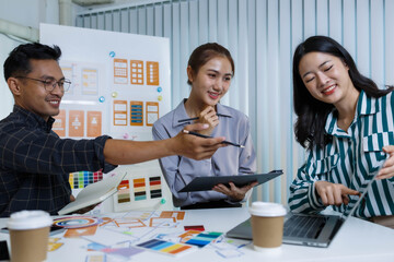 Fototapeta premium A man and two women are sitting at a table with a white background. The man is drawing on a white board while the women look on. Scene is collaborative and creative 