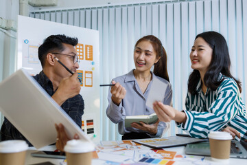 A man and two women are sitting at a table with a white background. The man is drawing on a white board while the women look on. Scene is collaborative and creative
