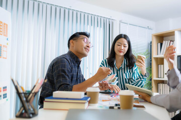 Obraz premium A man and two women are sitting at a table with a white background. The man is drawing on a white board while the women look on. Scene is collaborative and creative 
