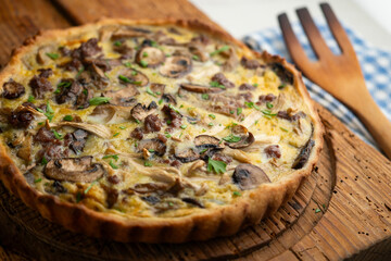 French quiche with wild mushrooms, egg, and beef on a wooden table.