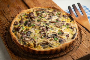 French quiche with wild mushrooms, egg, and beef on a wooden table.